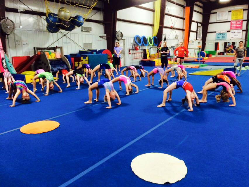 Several school-aged gymnasts do backbends under the watchful eye of our instructors